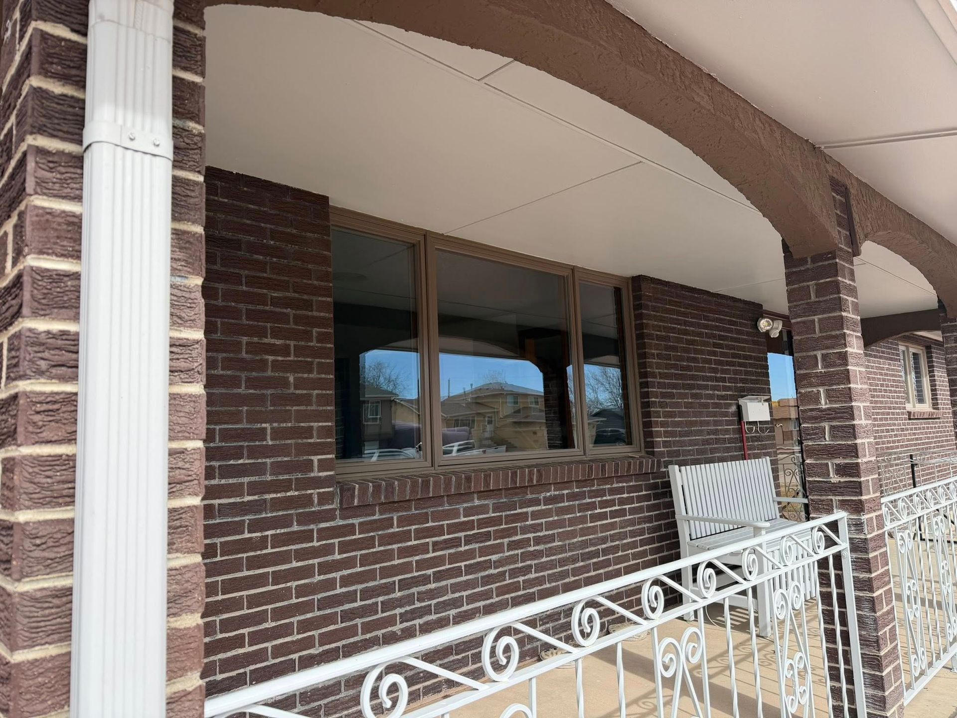 Brick house porch with white railing, brown columns, and a window under an arched overhang