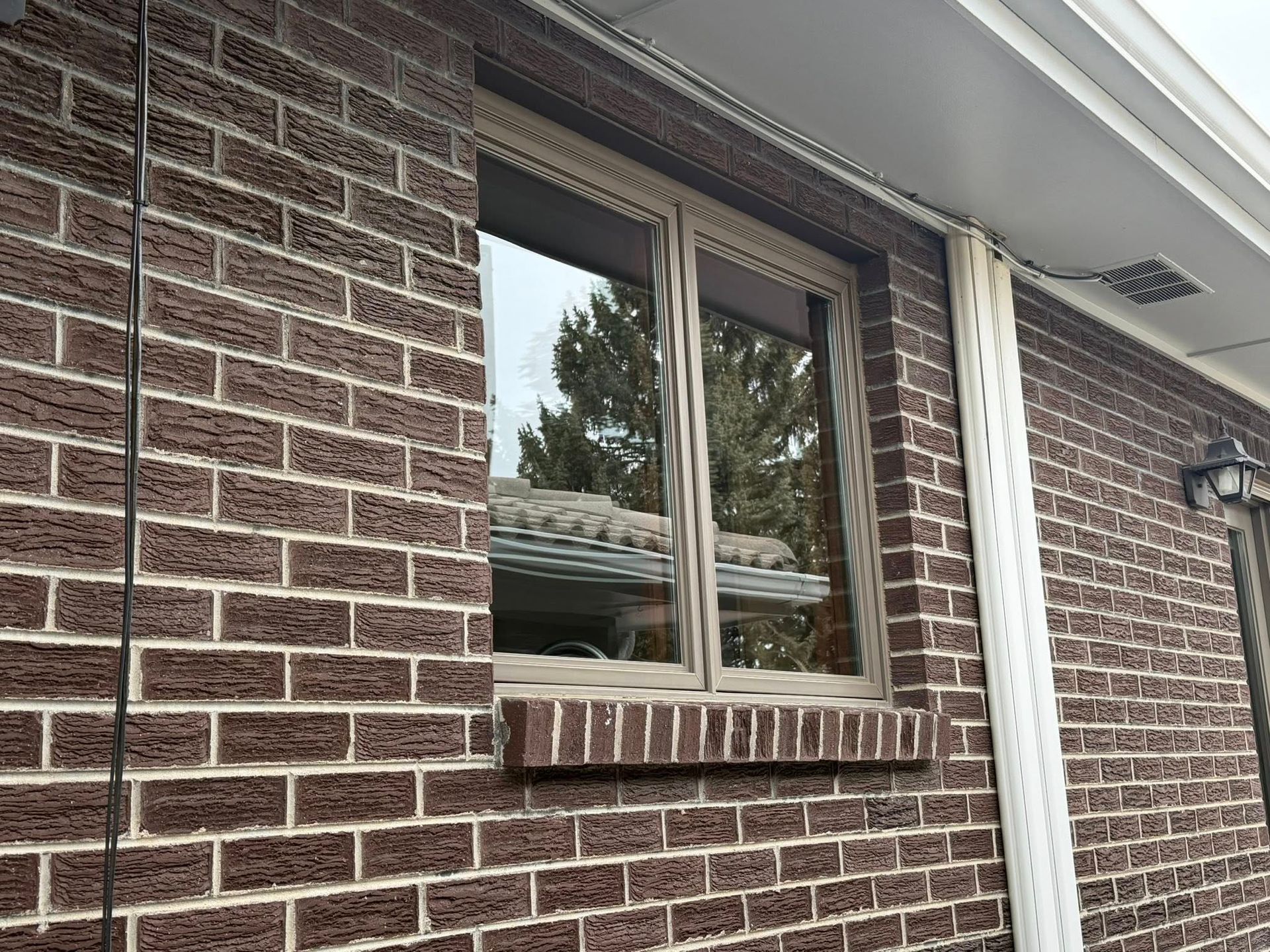 Brick house exterior with a window and white trim reflected in the glass