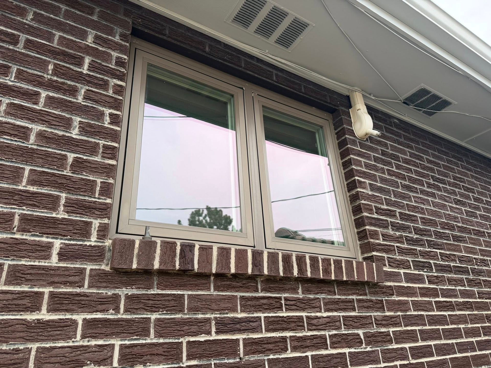 Brick house exterior with a small double-pane window and white soffit vents above it.