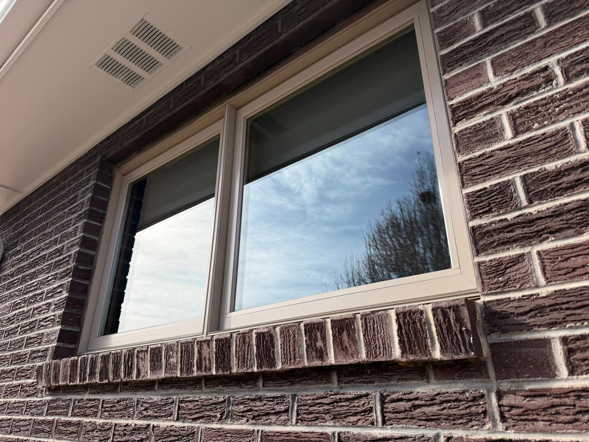Brick house window with white trim reflecting the sky and nearby trees