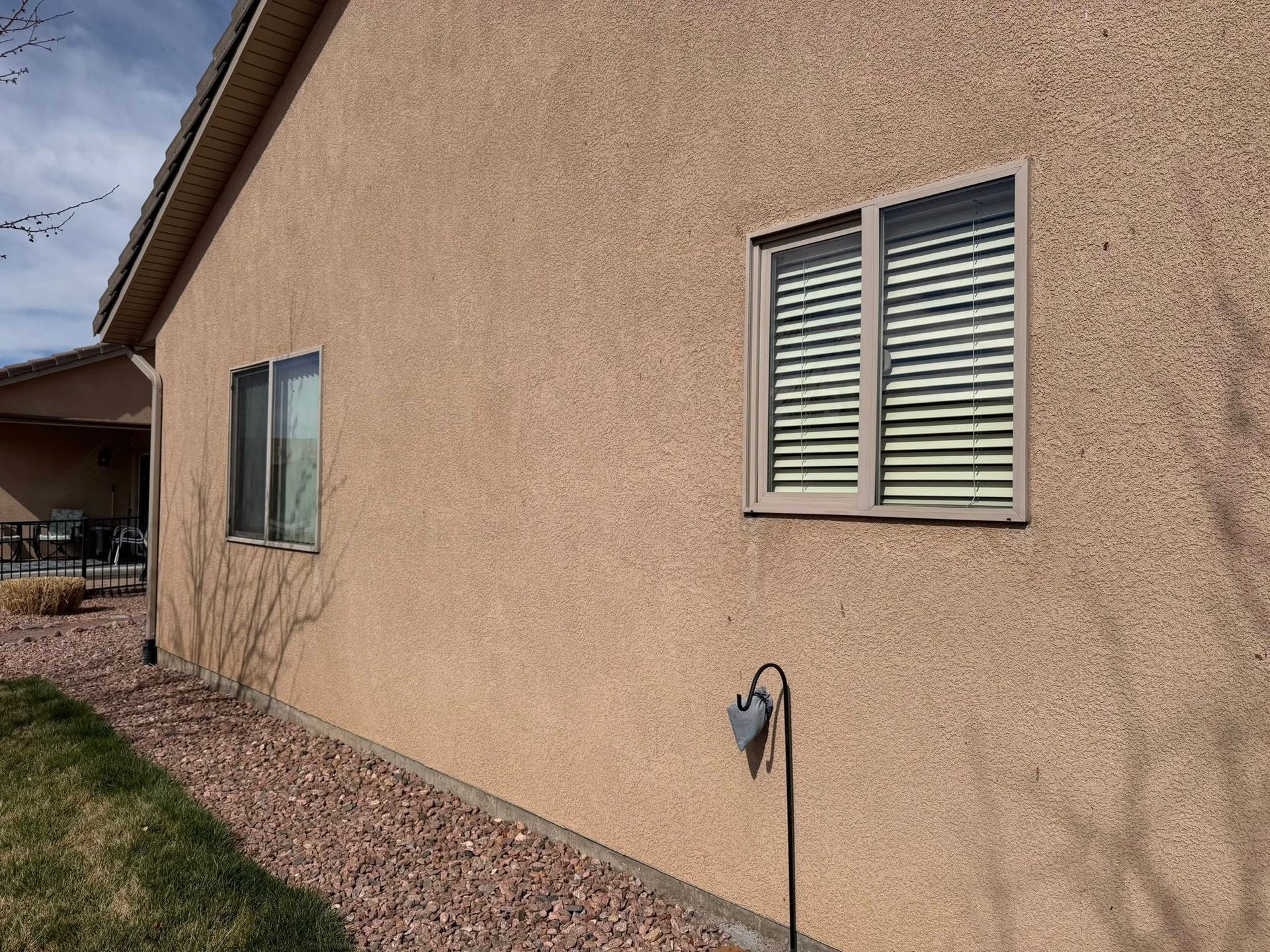 Beige stucco house exterior with two windows and a small lawn beside a gravel path.