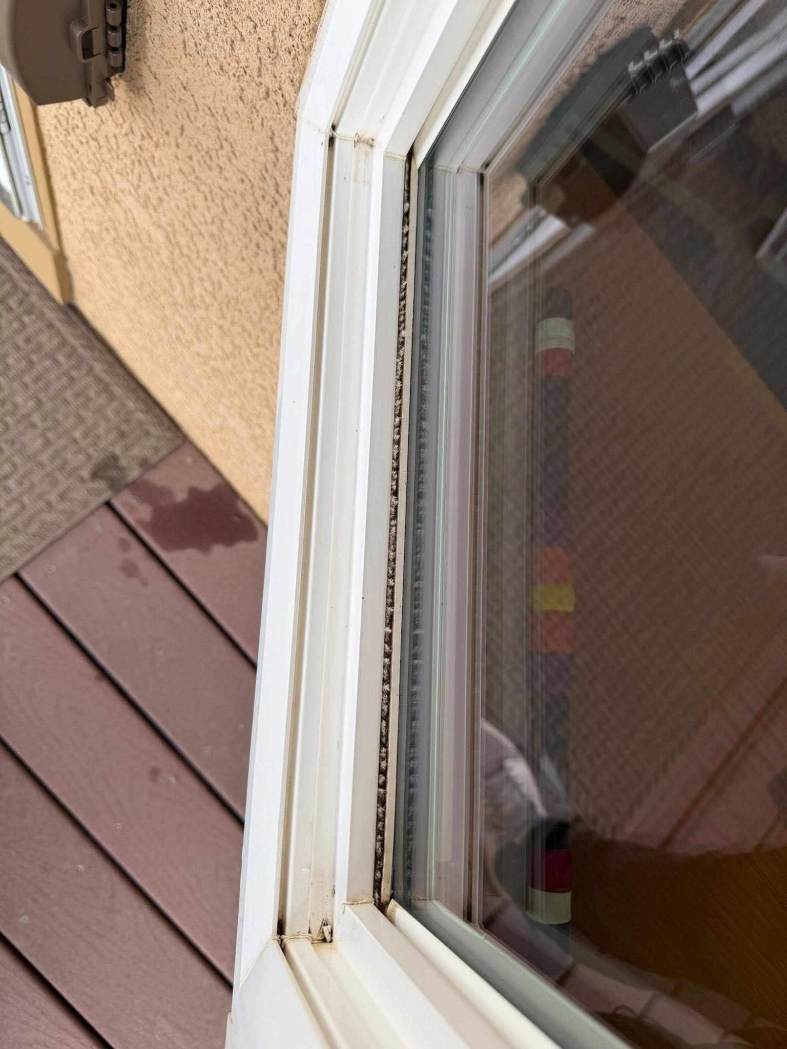 Close-up of a white window frame with peeling paint beside tan stucco and brown deck boards.