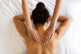 Person receiving a back massage on a white bed. Hands massage shoulders.