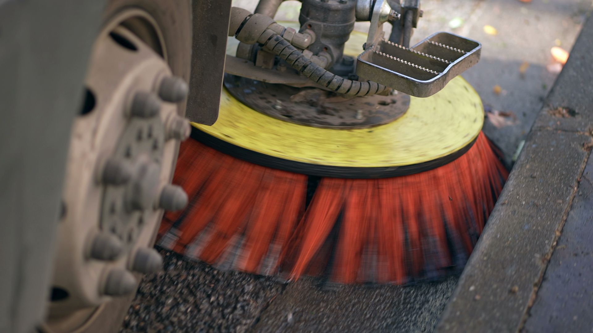 Street sweeper brush cleaning curbside pavement beside a road. Street sweeper brush cleaning curbside pavement beside a road.