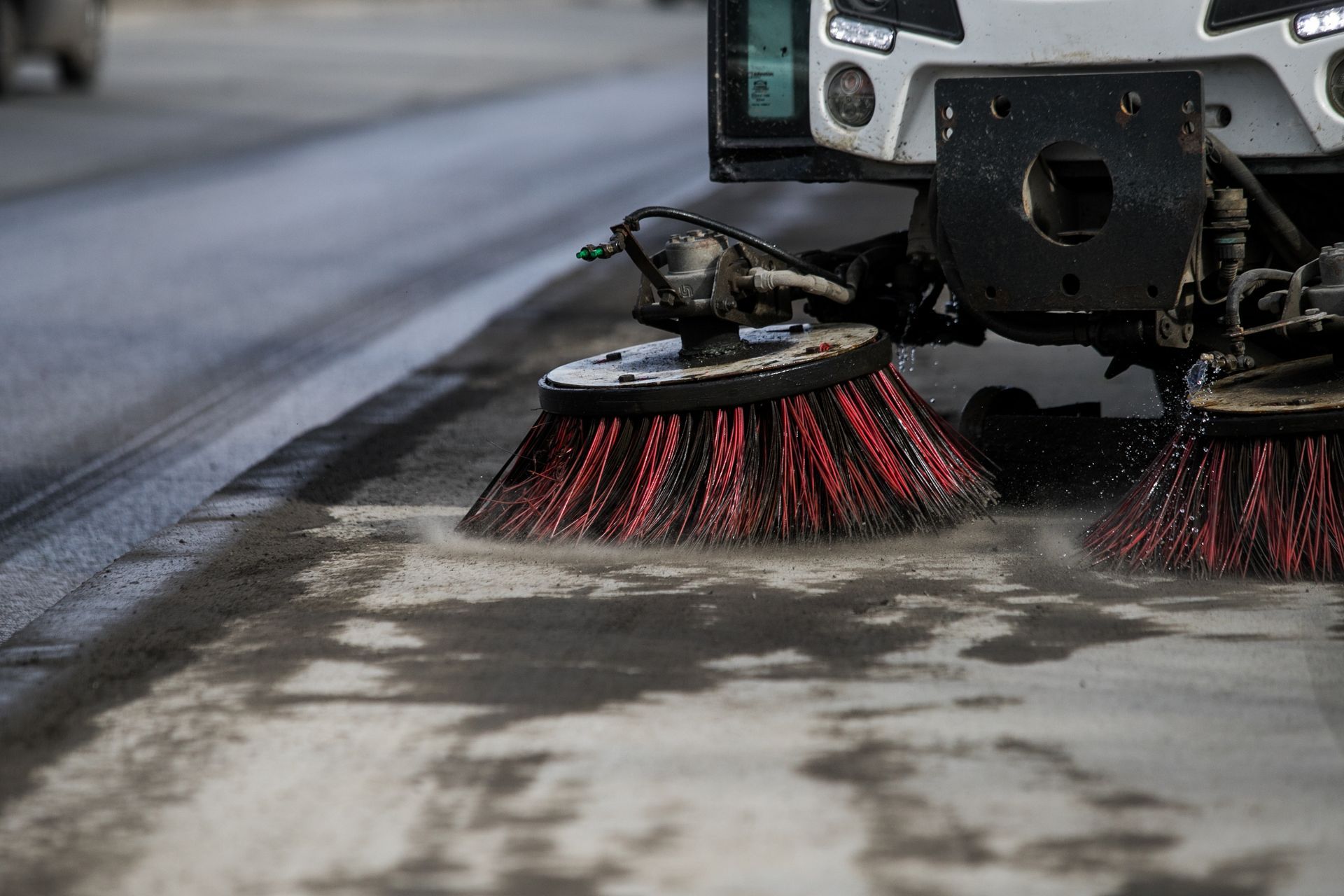Street sweeper brushes cleaning a roadway edge with water spray. Street sweeper brushes cleaning a roadway edge with water spray.