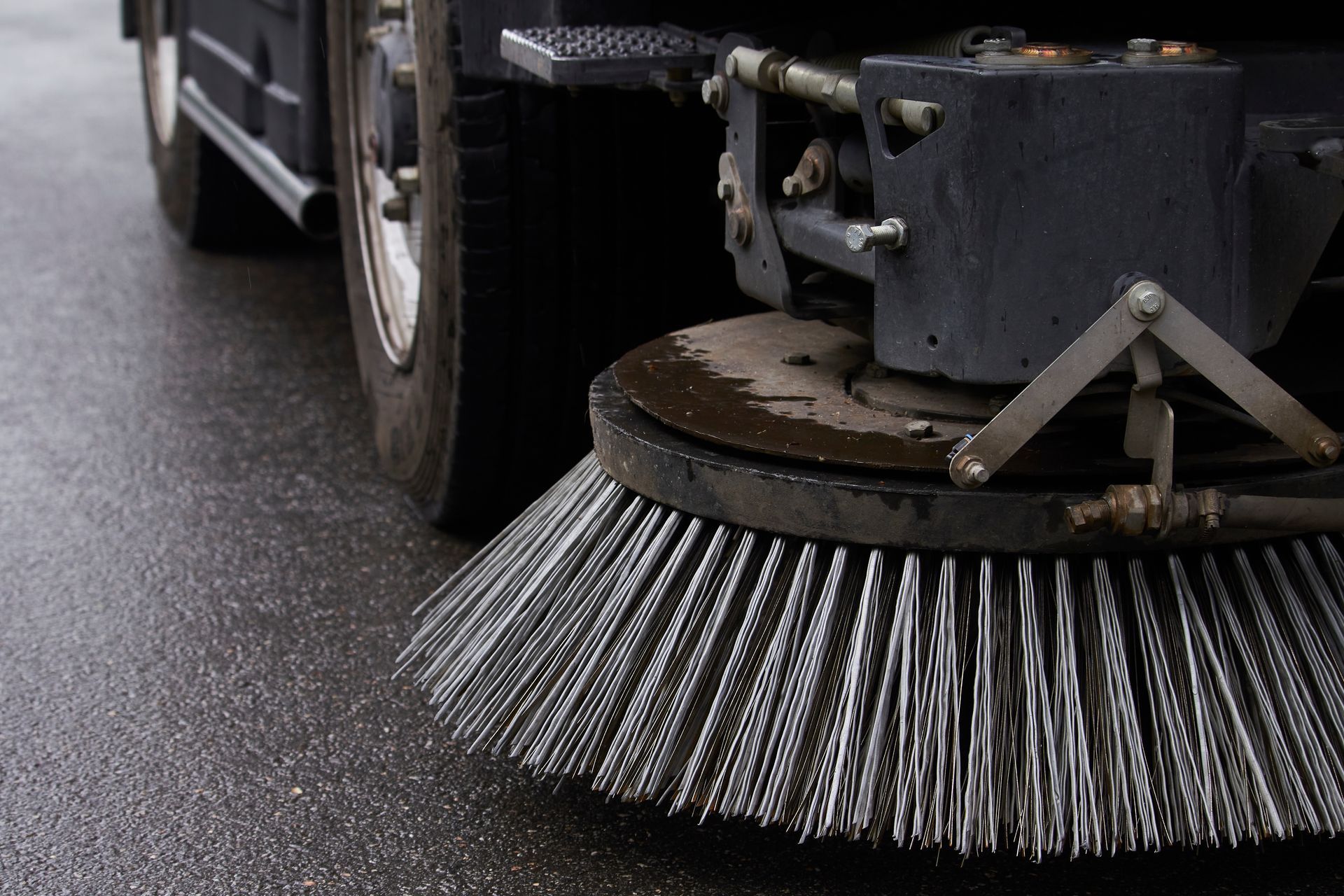 Close-up of a street sweeper brush cleaning wet pavement beside a vehicle.