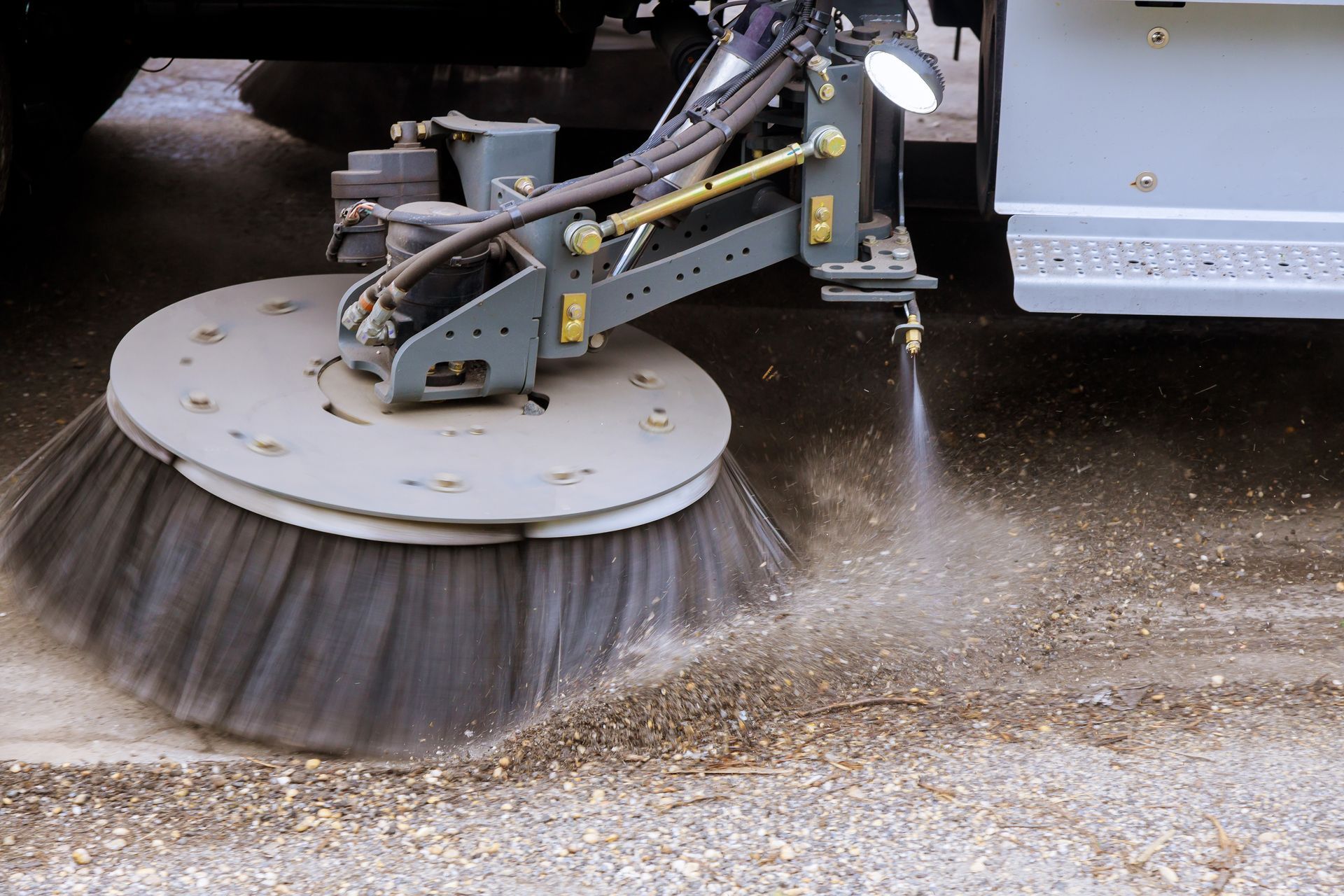 Rotating street sweeper brush clearing debris with water spray on pavement. Rotating street sweeper brush clearing debris with water spray on pavement.