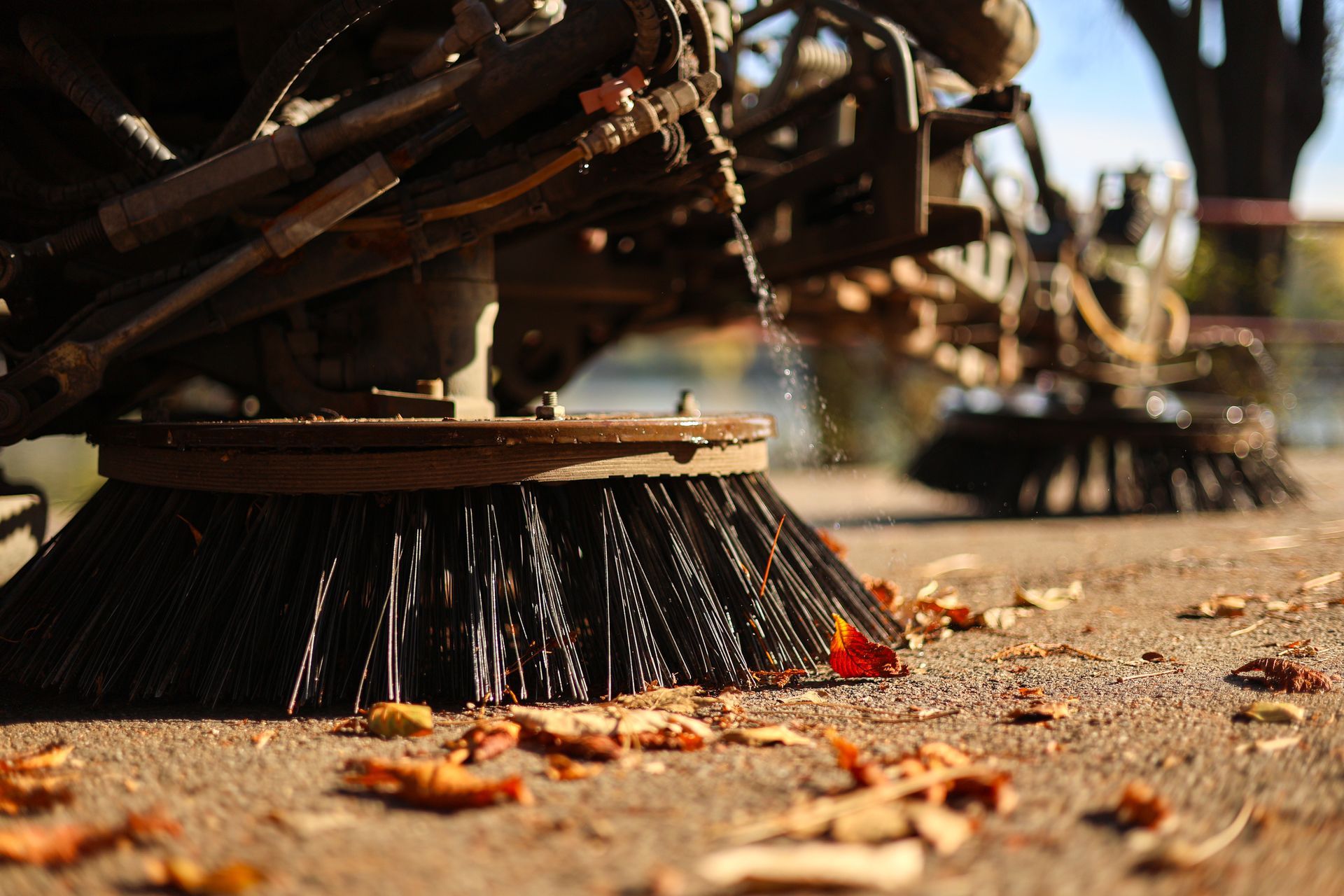 Close-up of a mechanical sweeper brush removing leaves and debris from pavement. Close-up of a mechanical sweeper brush removing leaves and debris from pavement.