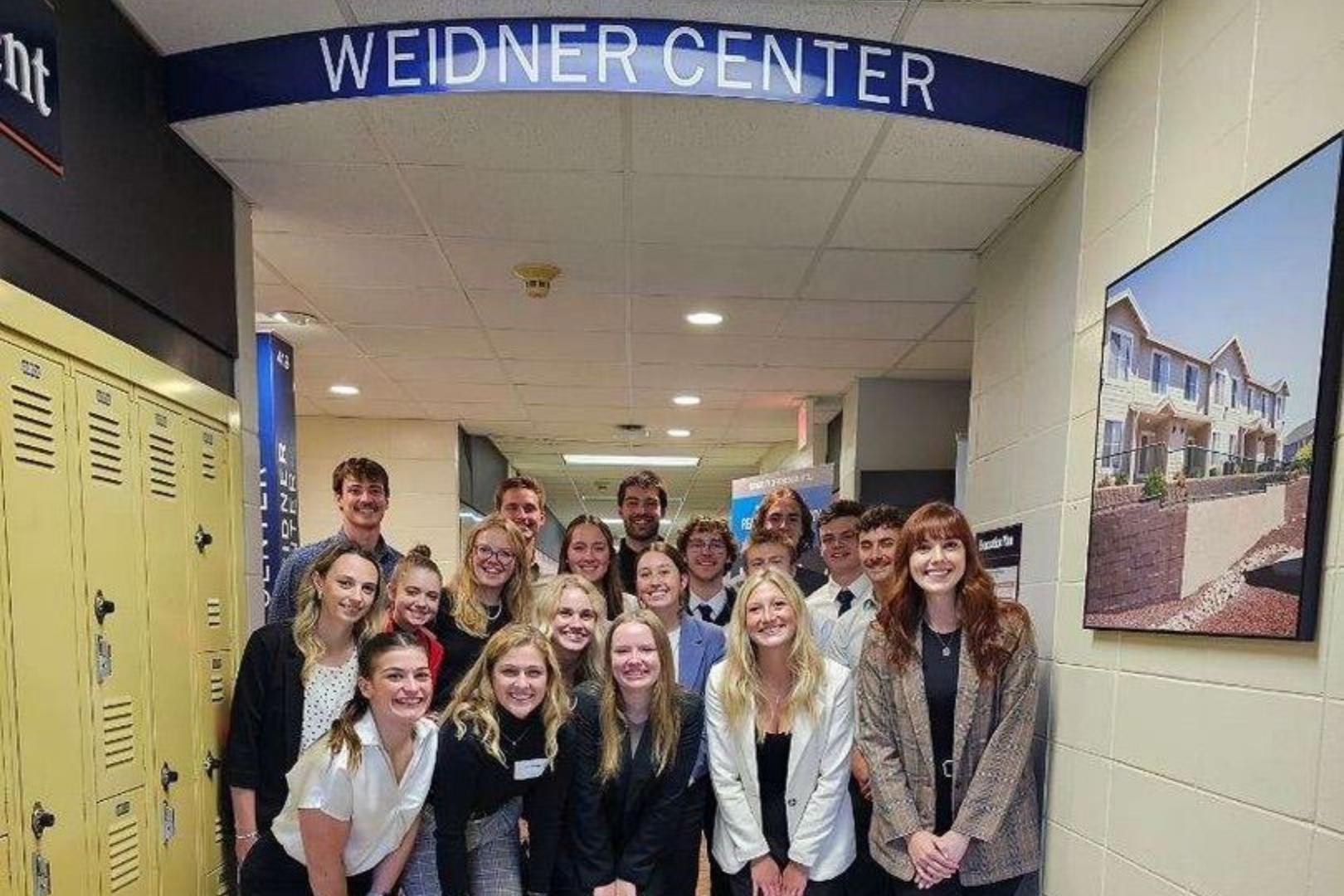 A group of students smiling in a hallway under a sign that reads 