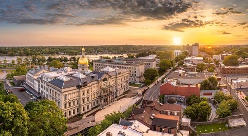 Aerial view of a historic town center at sunset, with a golden-domed building and streets lined with trees.