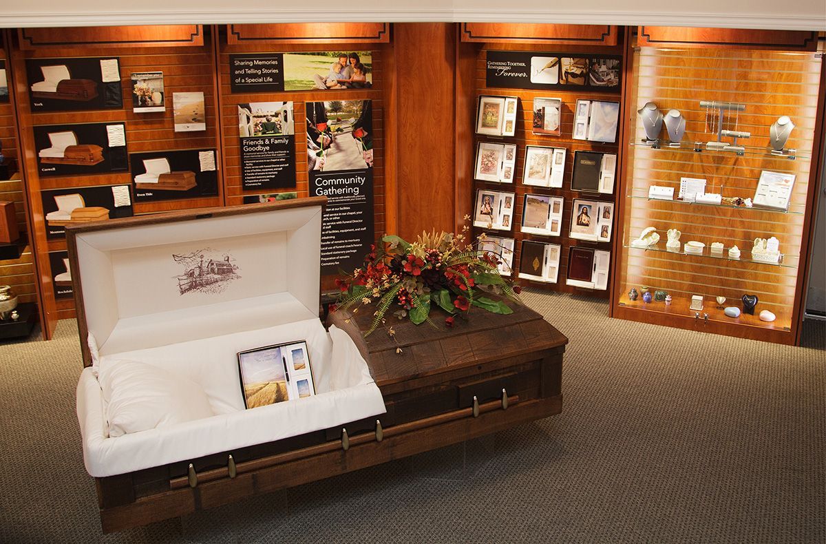 Open white casket in a funeral home showroom with floral arrangement and display cabinets on wood-paneled walls