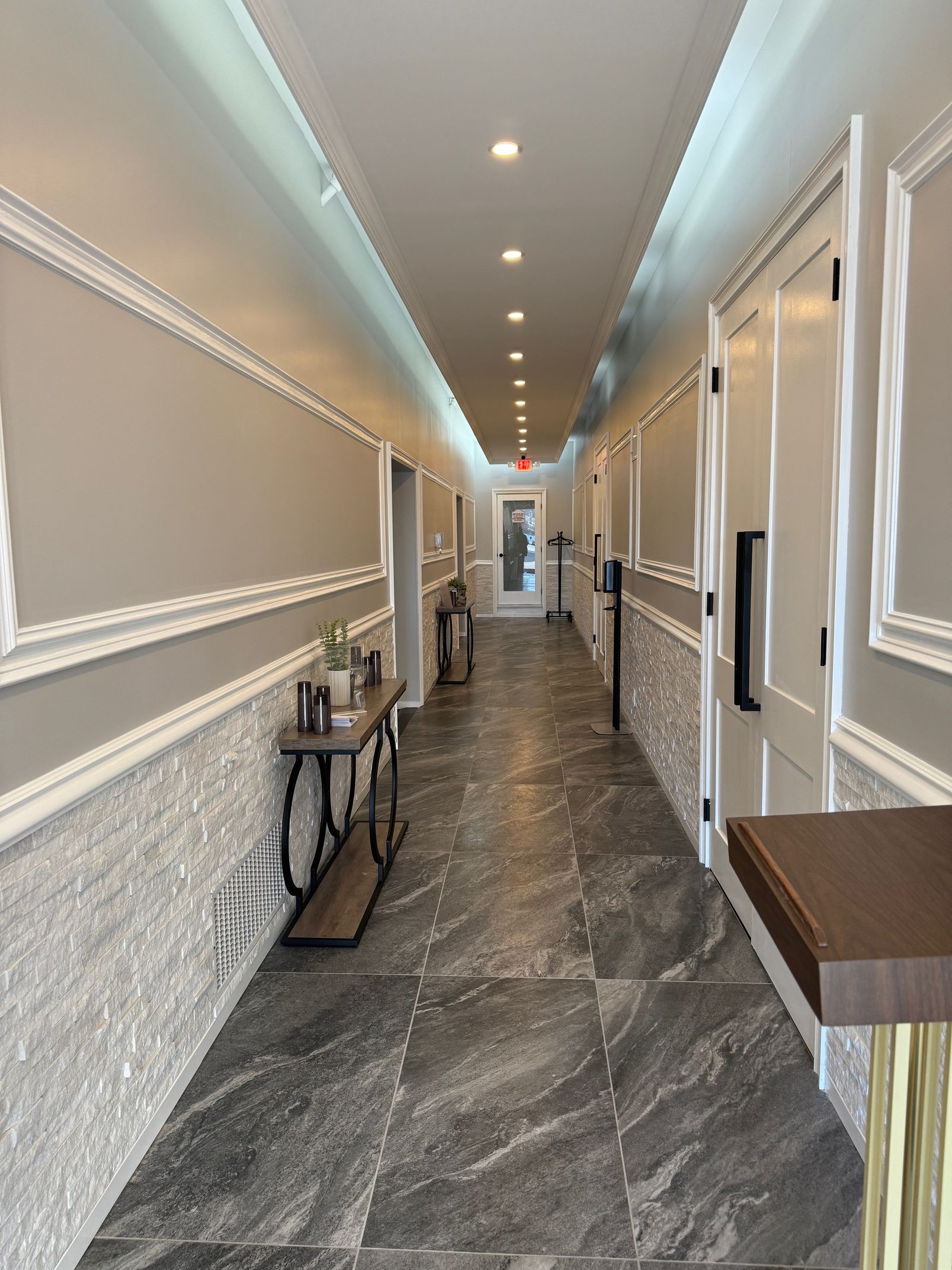 Elegant hallway with marble floors, white trim, wall sconces, and a narrow table at the end.
