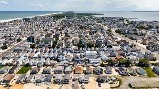 Aerial view of a coastal neighborhood with rows of houses, sandy beach, and ocean in the background.