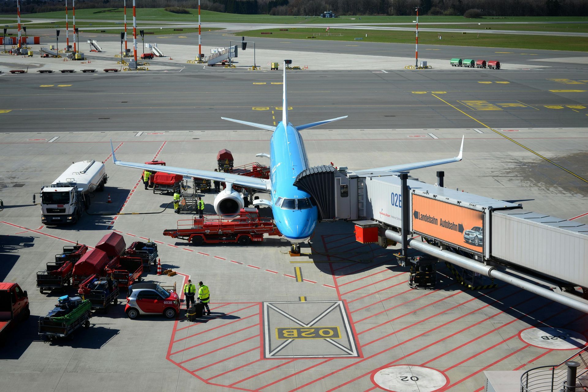 Blue airplane at an airport gate beside service vehicles and a jet bridge