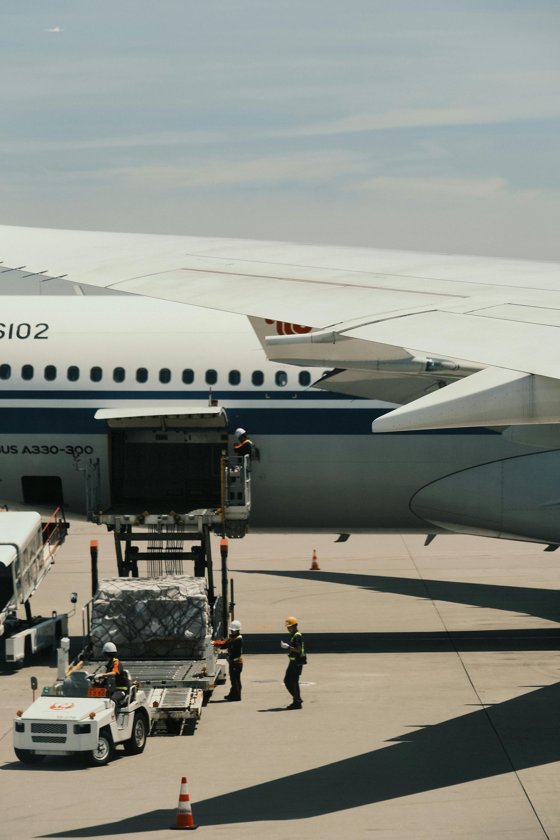 Airplane on tarmac with baggage loader and ground crew beneath the wing