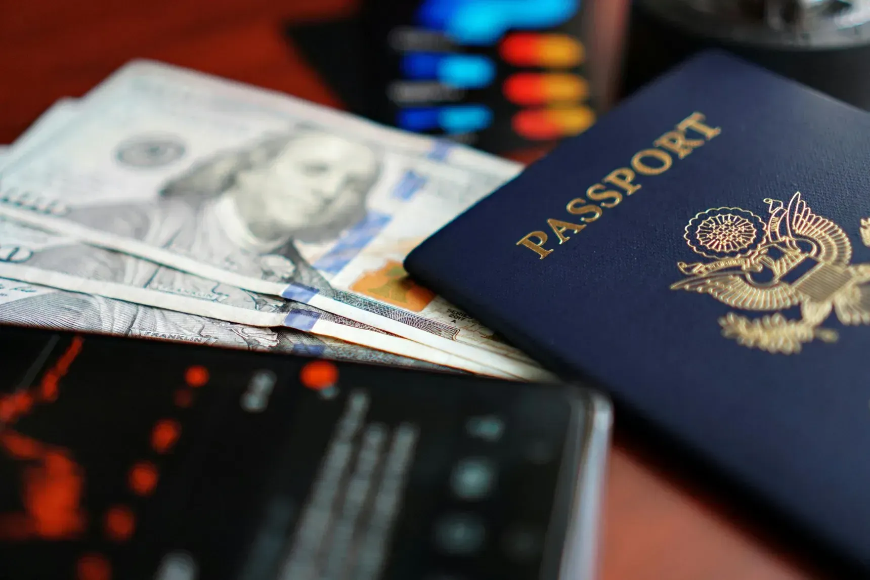 Passport, cash, and smartphone on a table with a blurred flight board in the background