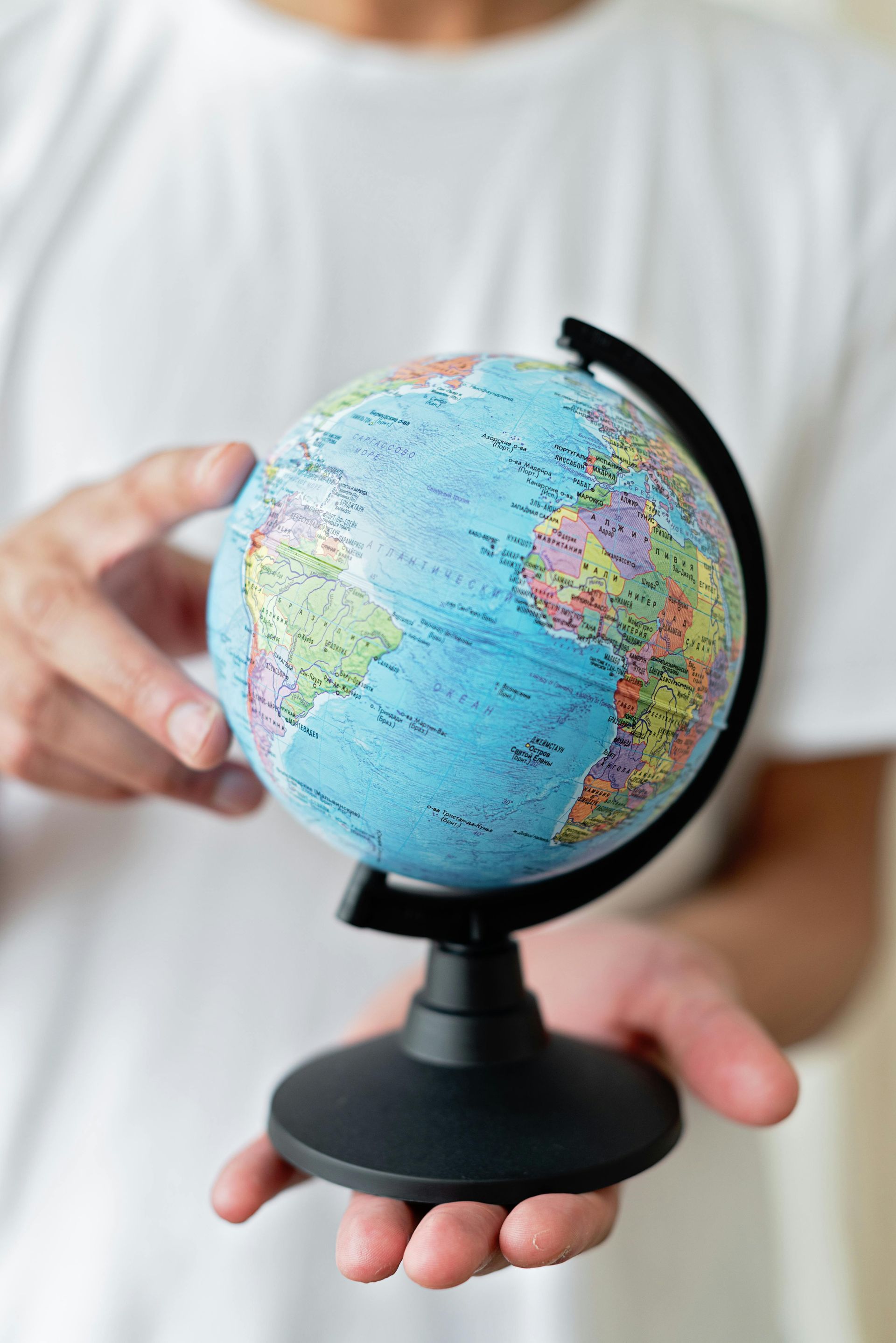 Small globe held in a person’s hands against a white shirt background