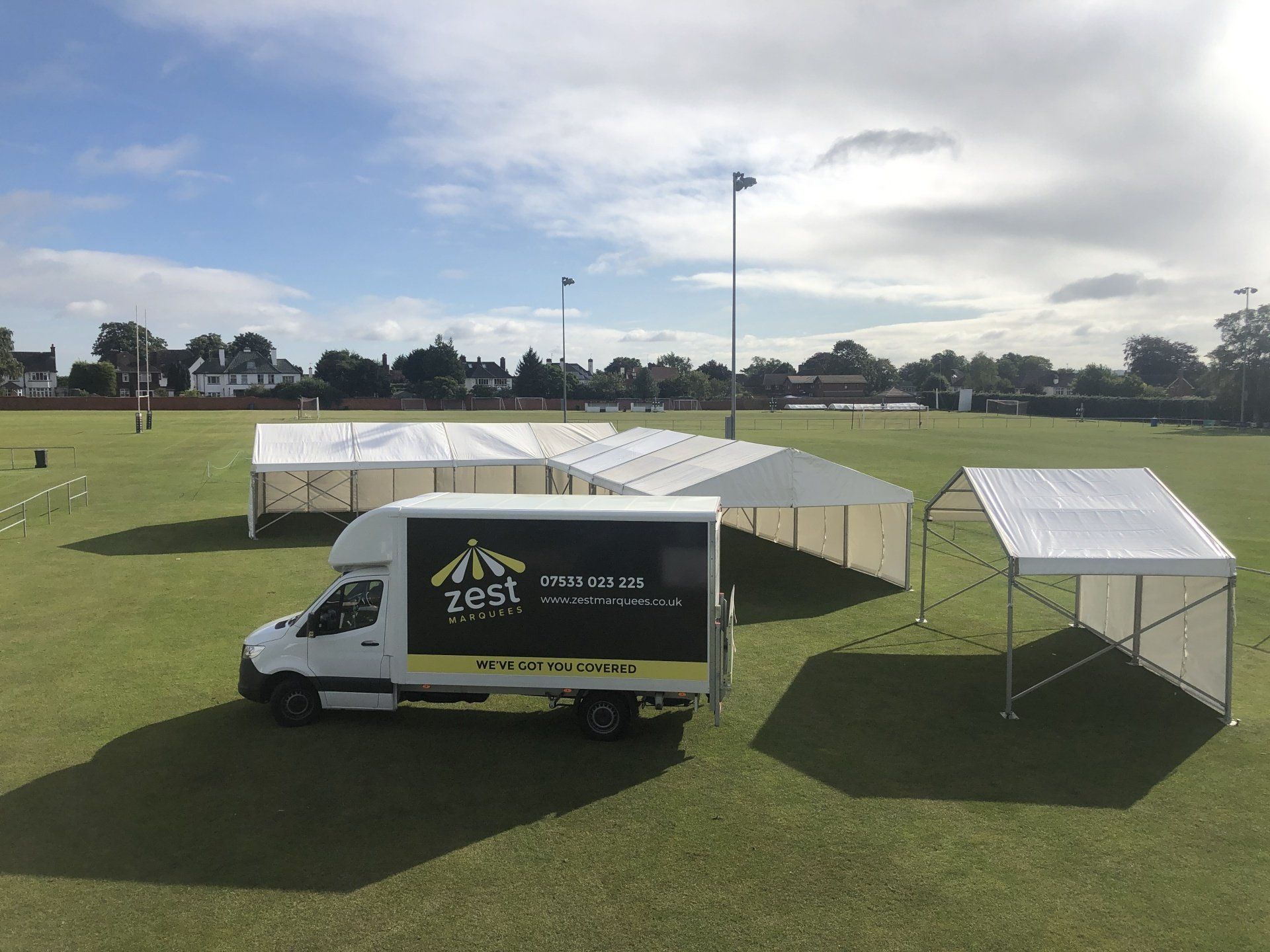 A white van is parked in a field next to tents.
