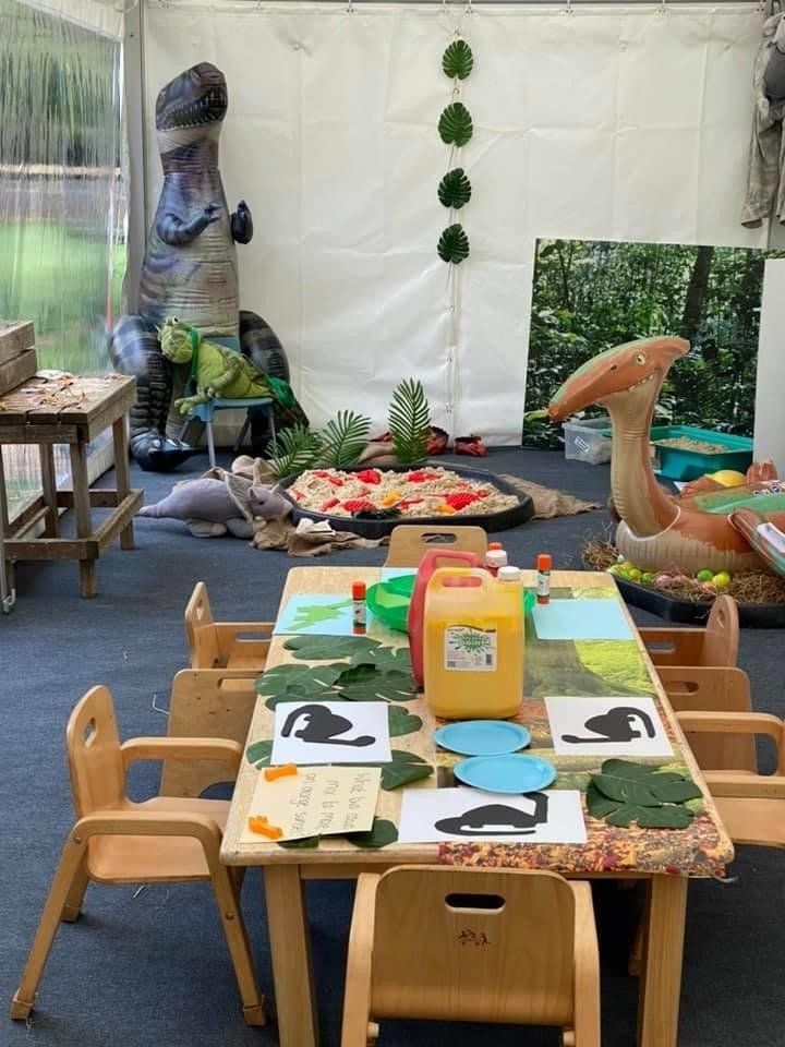 A table and chairs in a room with a dinosaur statue in the background.