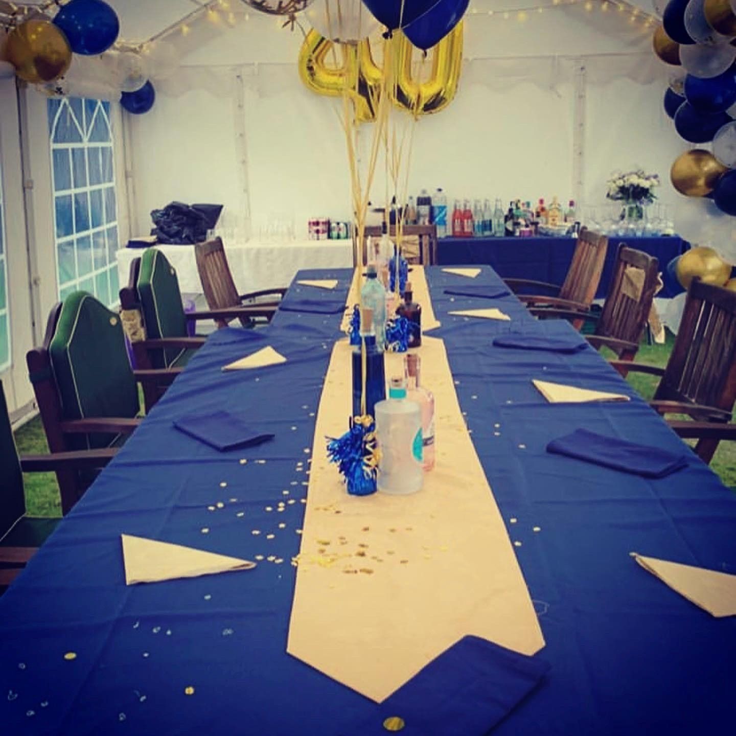 A long table with a blue table cloth and balloons on it