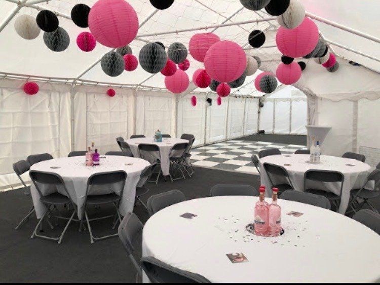 A tent with tables and chairs and pink and black lanterns hanging from the ceiling.