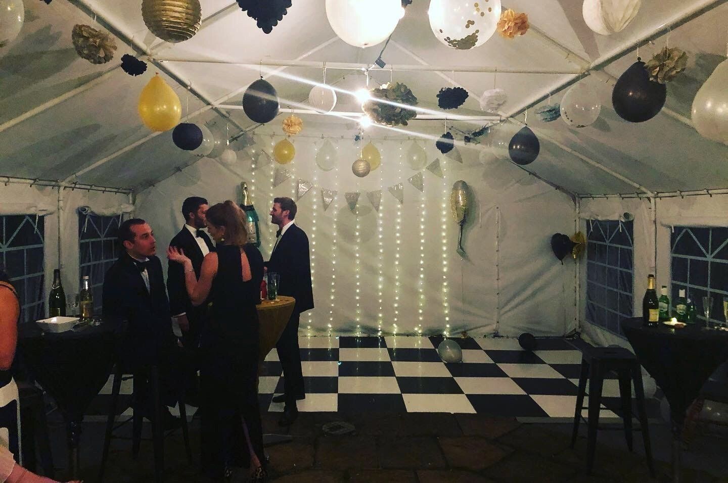 A group of people are standing on a checkered dance floor in a tent.