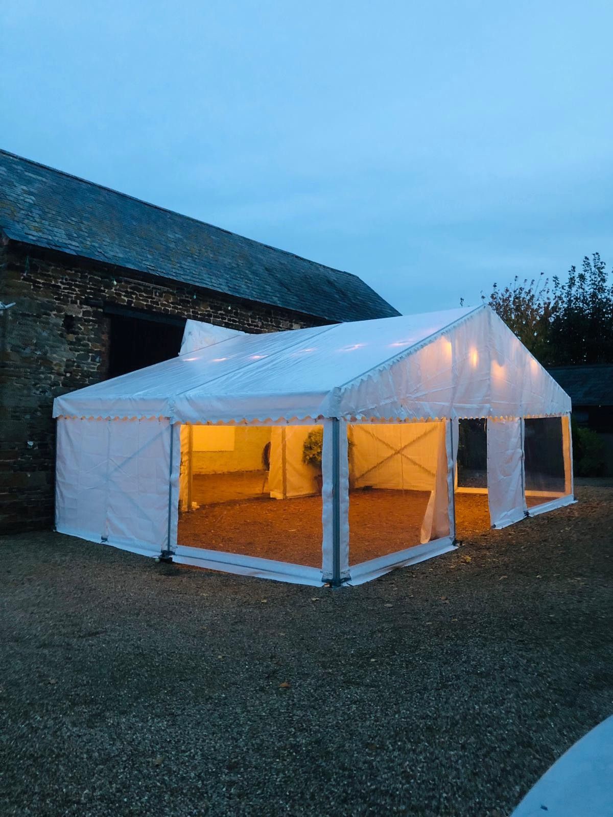 A large white tent is sitting in the dirt in front of a building.