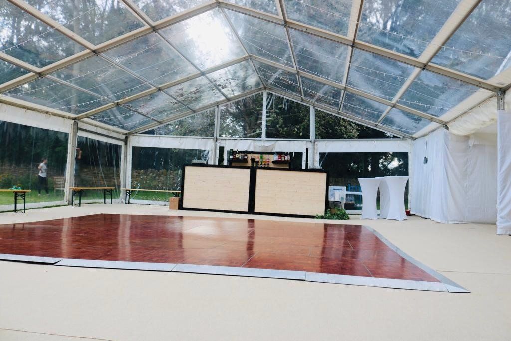A large clear tent with a wooden dance floor underneath it