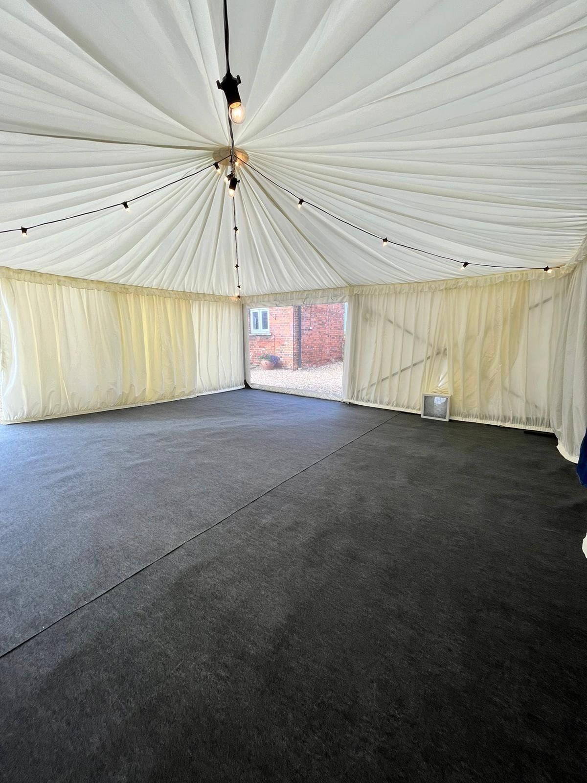 A large empty tent with a black carpet and white curtains.