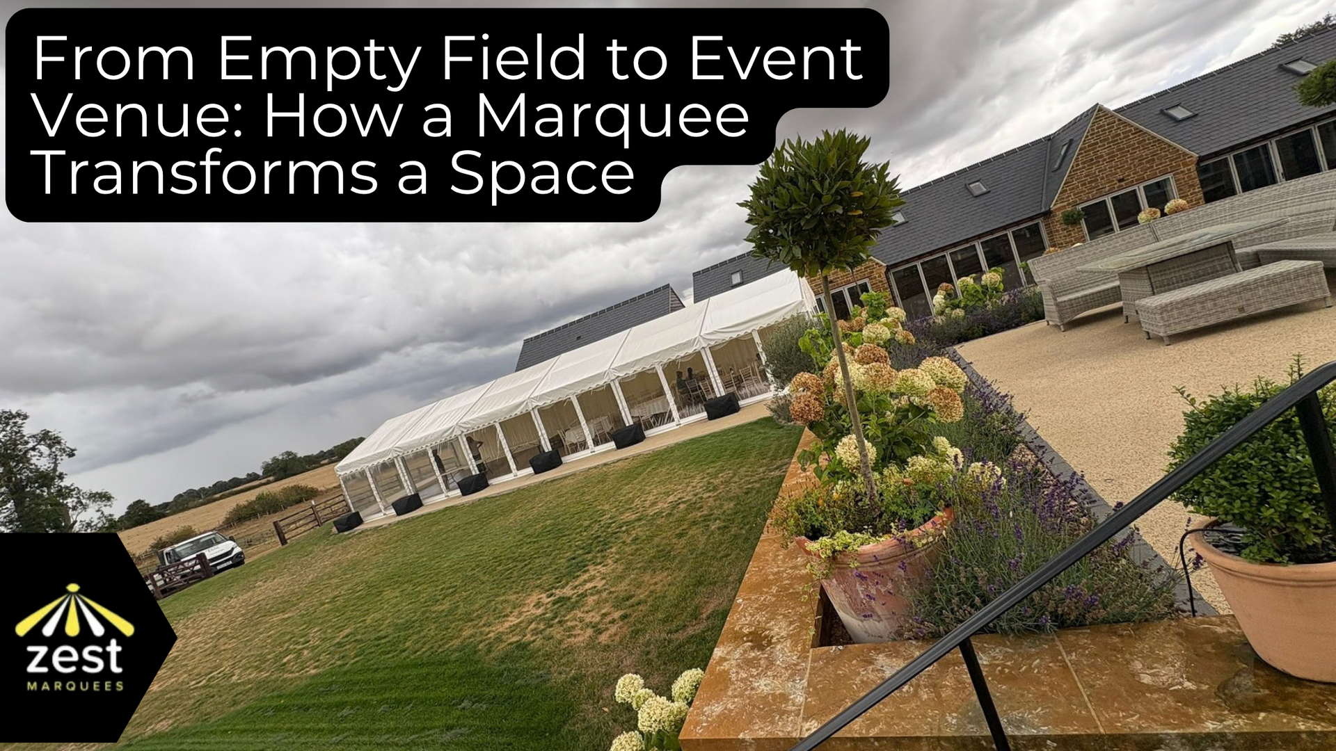 Marquee on a grassy field beside a farmhouse, with potted plants and event setup in progress