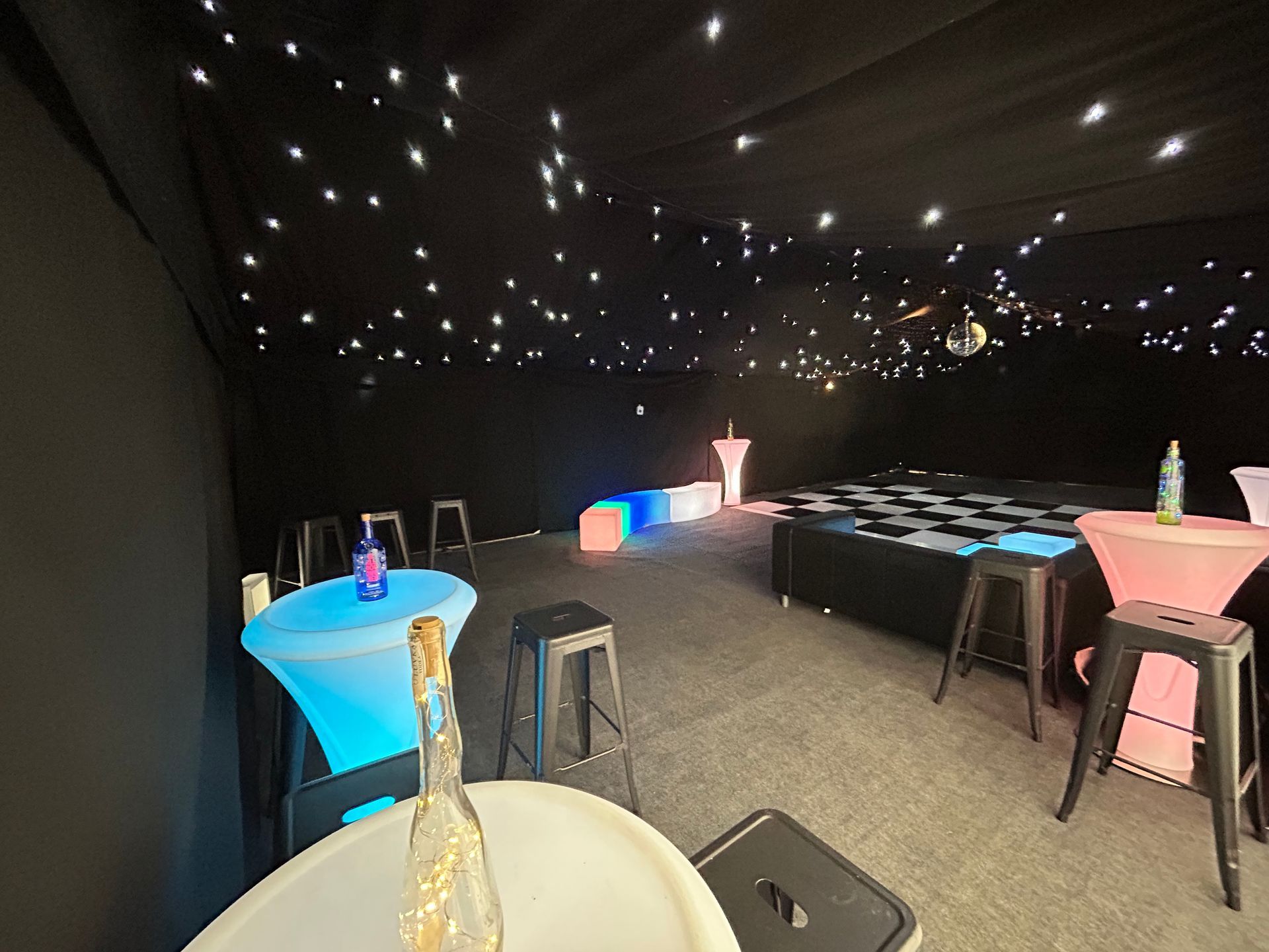 A room with tables and stools and a bottle of champagne on a table.