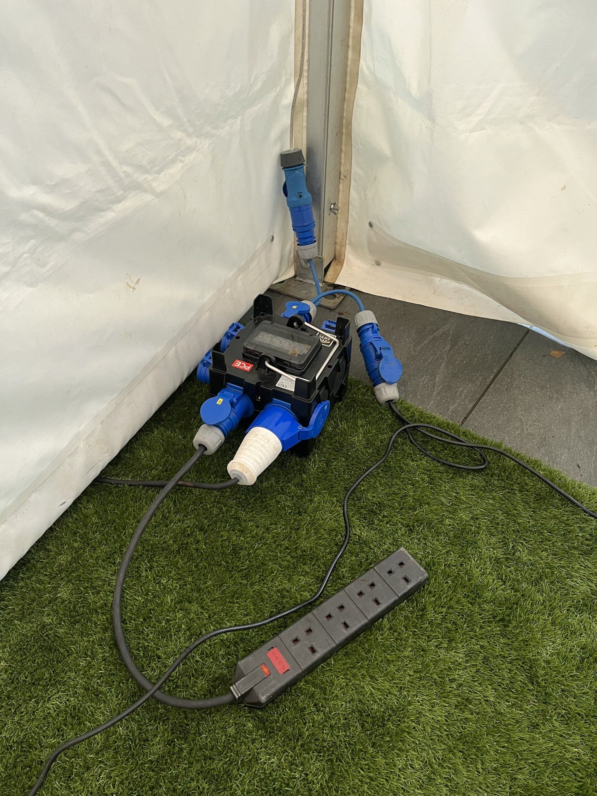 A power strip is sitting on the grass next to a tent.