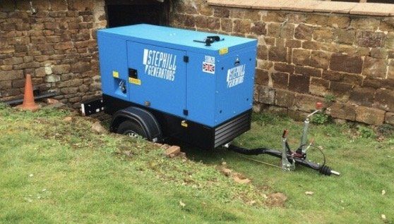 A blue generator is sitting on a trailer in front of a brick wall.