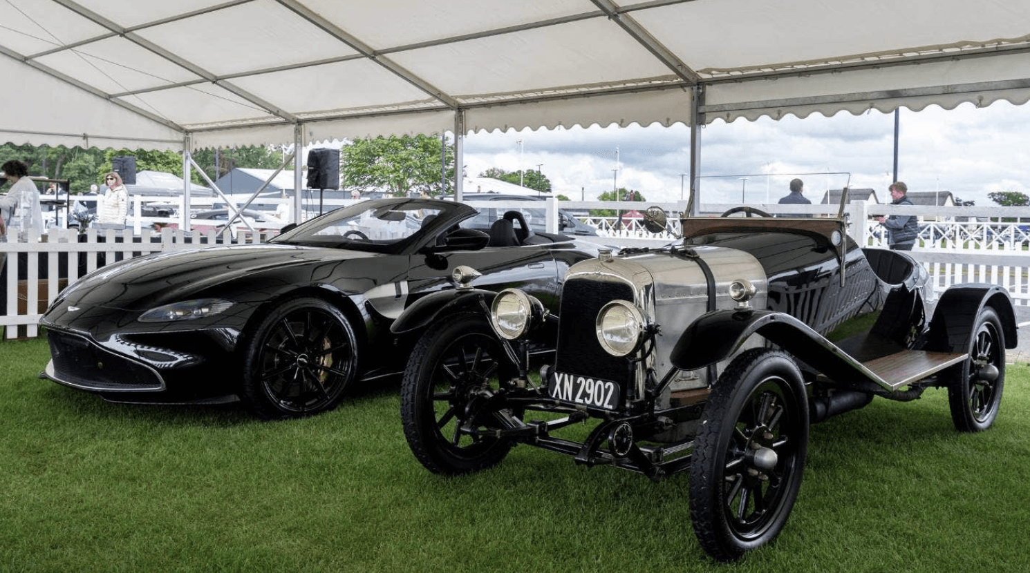 Two old cars are parked next to each other under a tent.