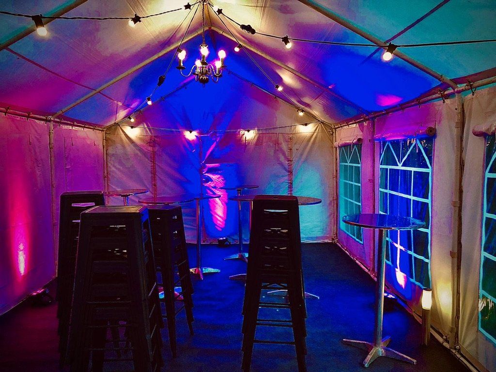 A tent with tables and chairs inside of it is lit up with blue and purple lights.