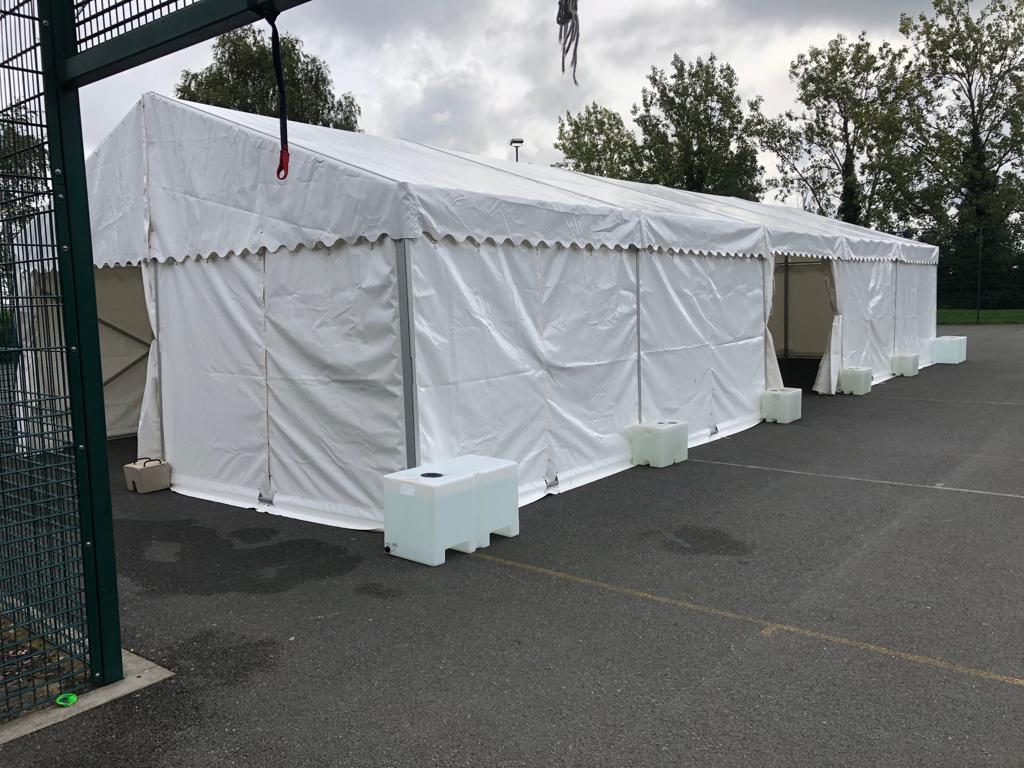 A row of white tents are lined up in a parking lot.