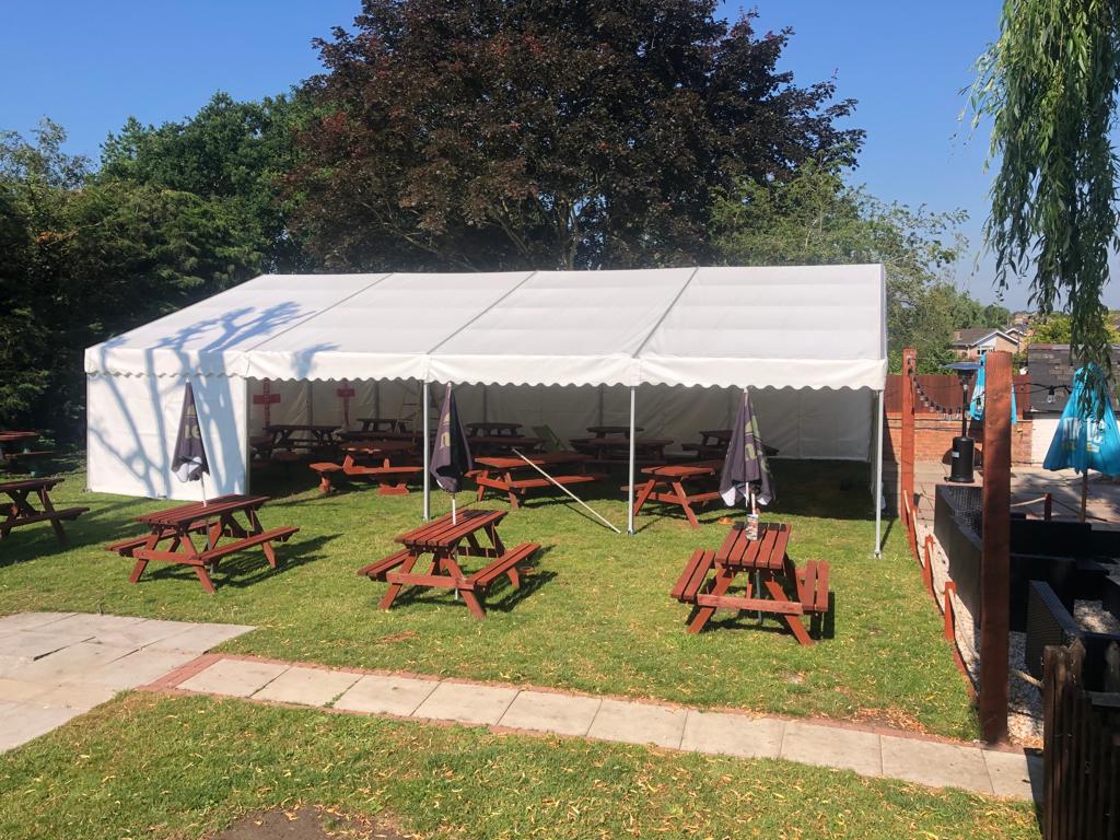 A large white tent with wooden picnic tables underneath it.