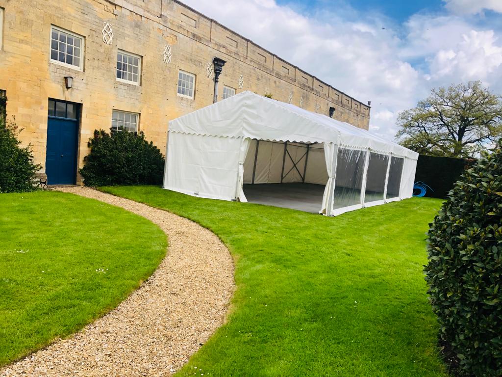 A large white tent is sitting in the grass in front of a building.