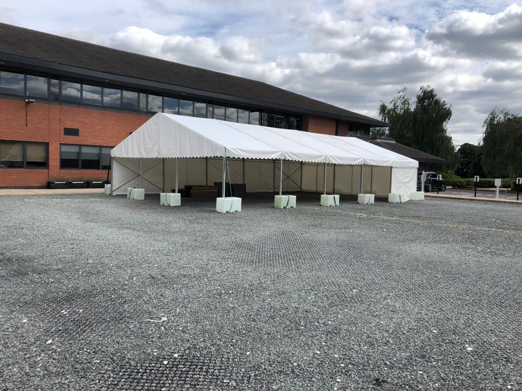 A large white tent is sitting in a gravel lot in front of a large building.