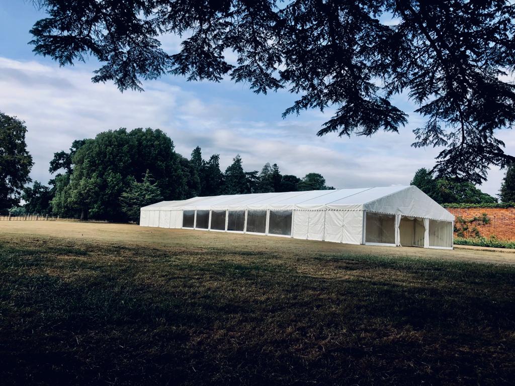 A large white tent is sitting in the middle of a field surrounded by trees.