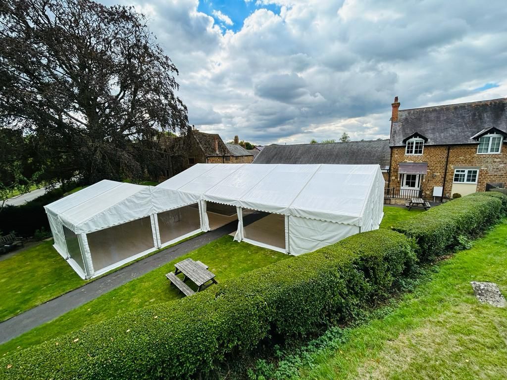 A large white tent is sitting in the grass in front of a house.