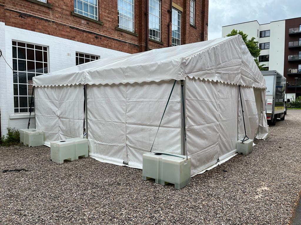 A white tent is sitting on a gravel driveway in front of a brick building.