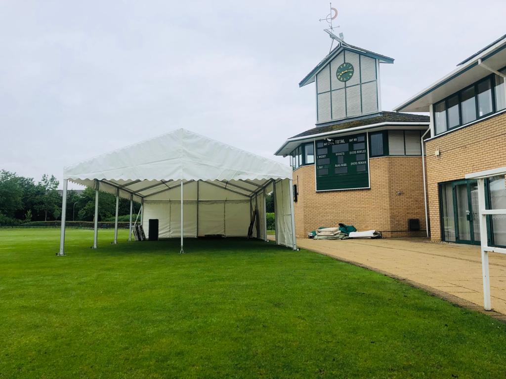 A large white tent is sitting in the grass in front of a building.