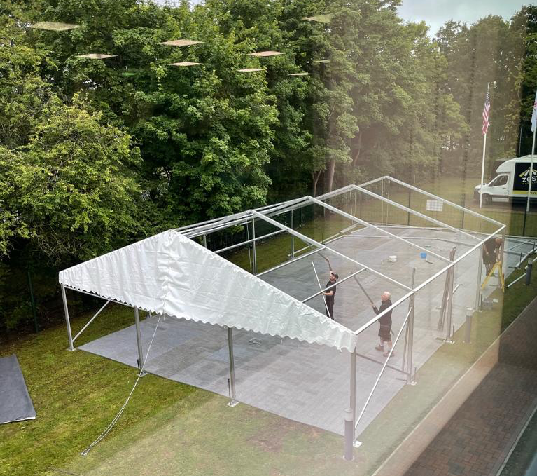 A large white tent is being built in a grassy field.