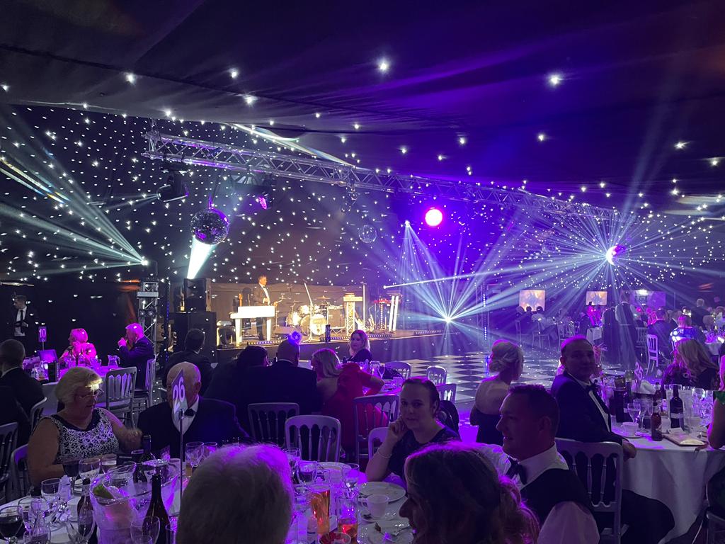 A group of people are sitting at tables in a room with purple lights.