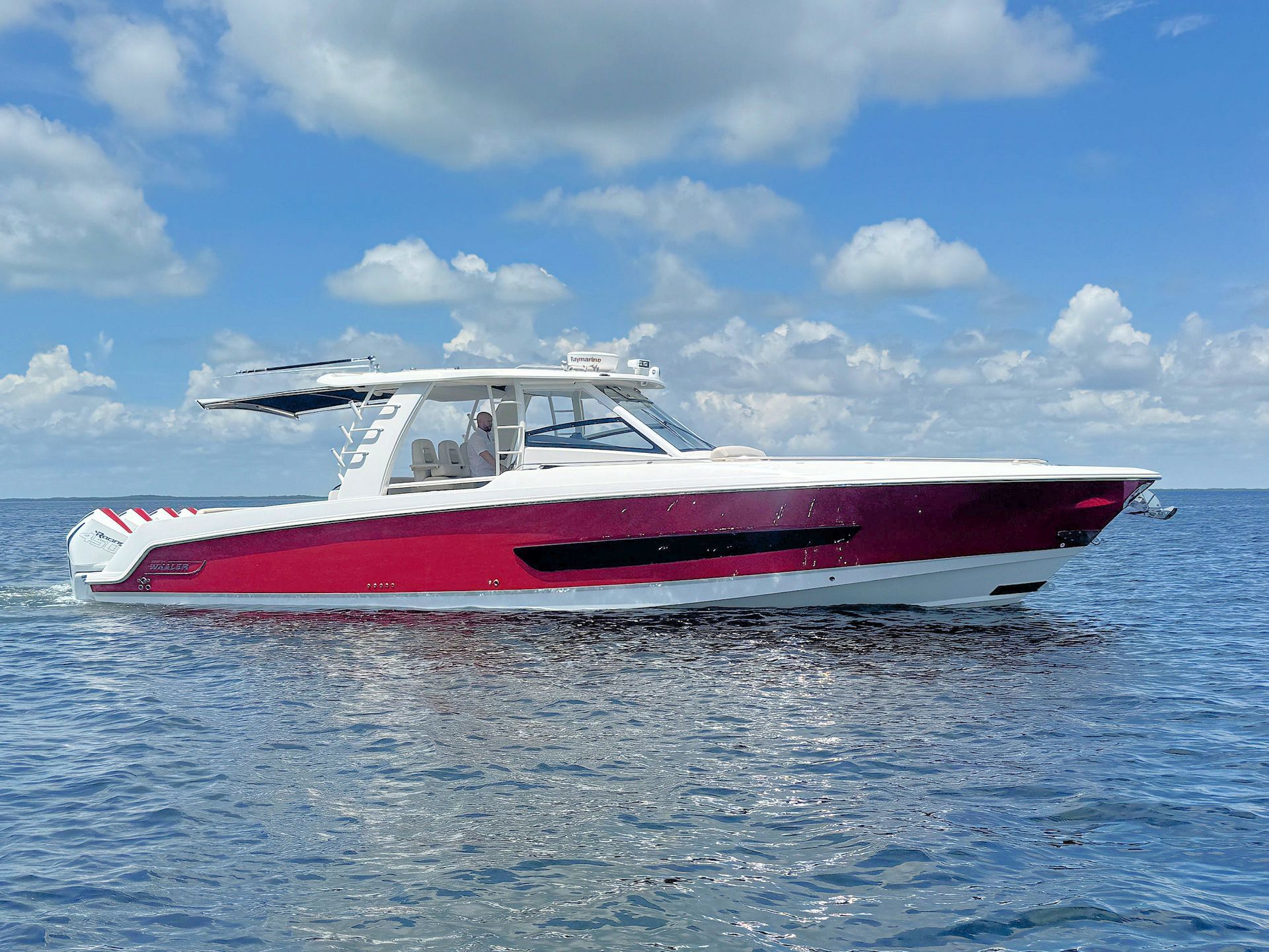 Red and white center console cruising on calm blue water under a partly cloudy sky