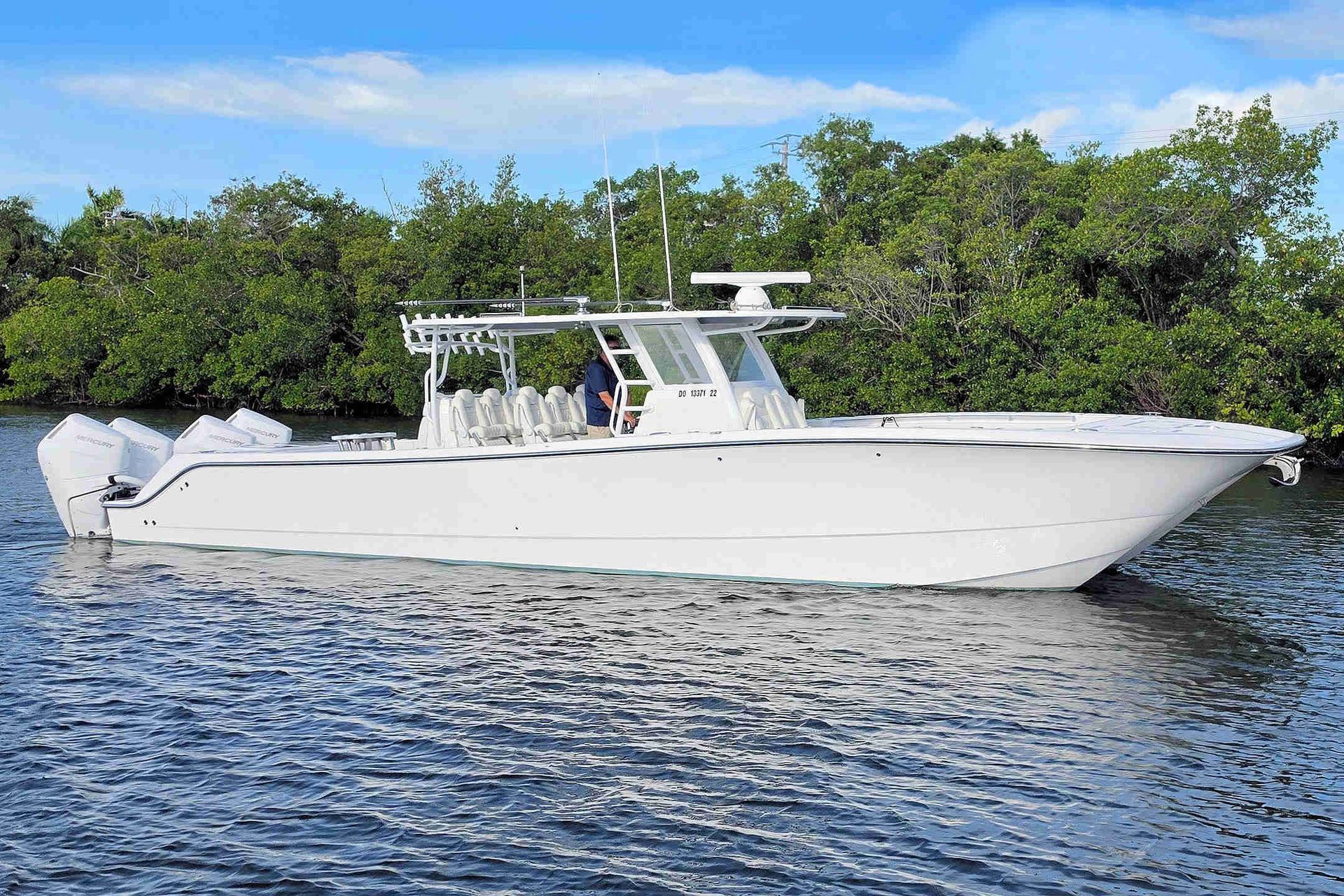 White center-console power catamaran cruising on calm water with green shoreline in the background