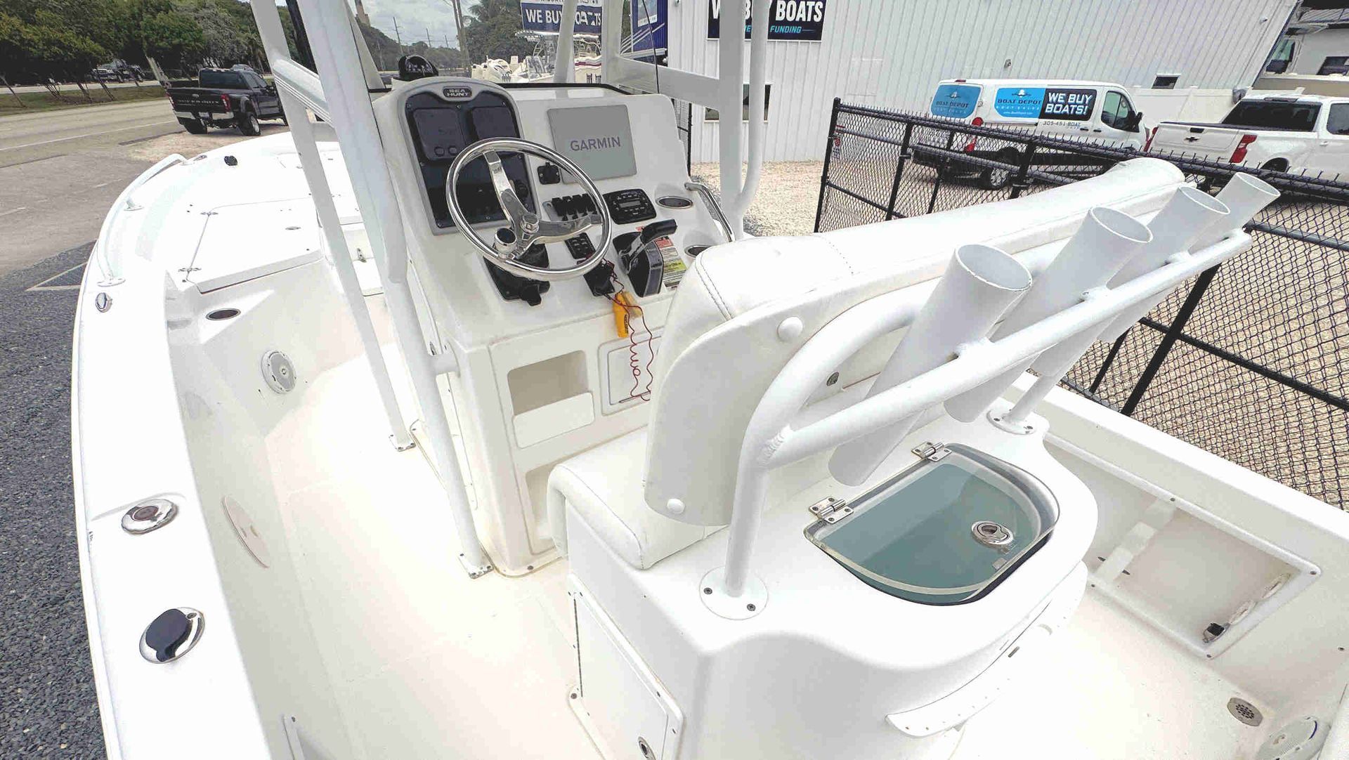 Boat cockpit with white seats and helm console, showing rod holders and storage on a clean deck.