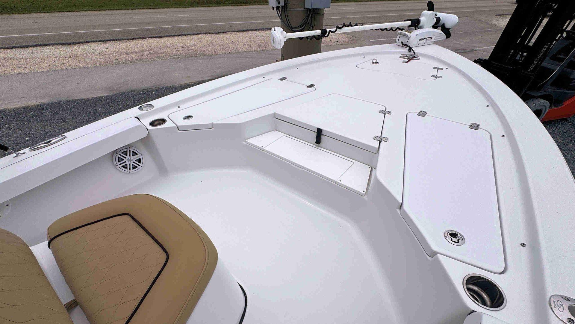 White boat bow with tan seat cushions and storage hatches on a calm dockside scene