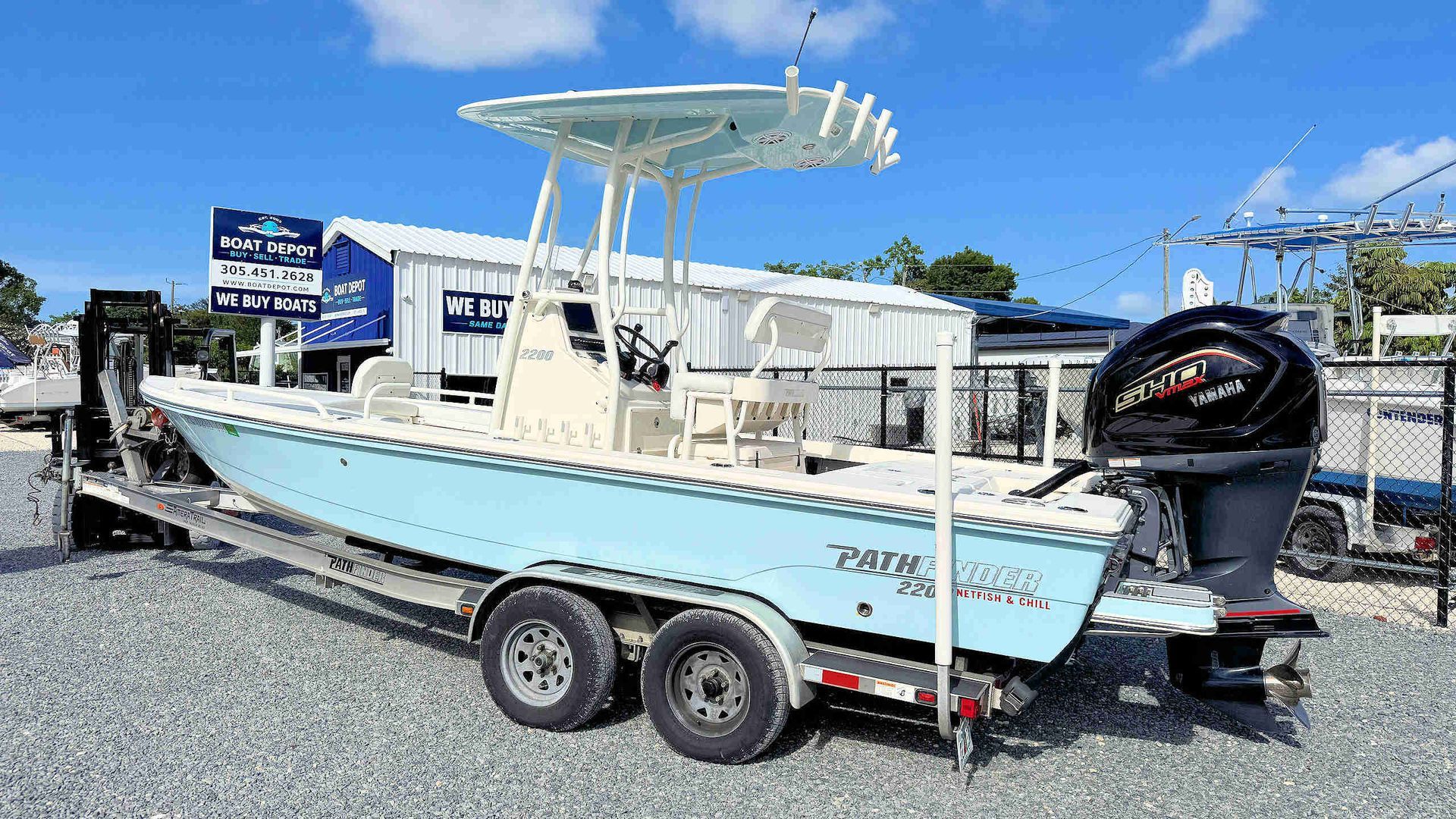 Light blue fishing boat on a trailer, parked outdoors under a clear sky.